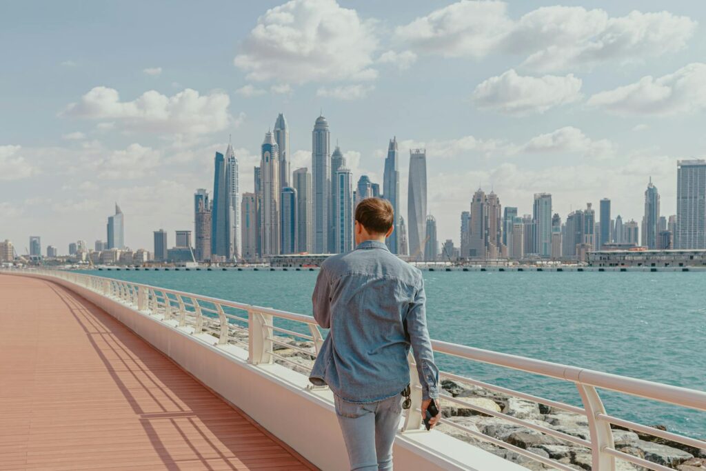 Vue arrière d'un homme marchant le long d'une promenade au bord de l'eau avec vue sur la marina de Dubaï.