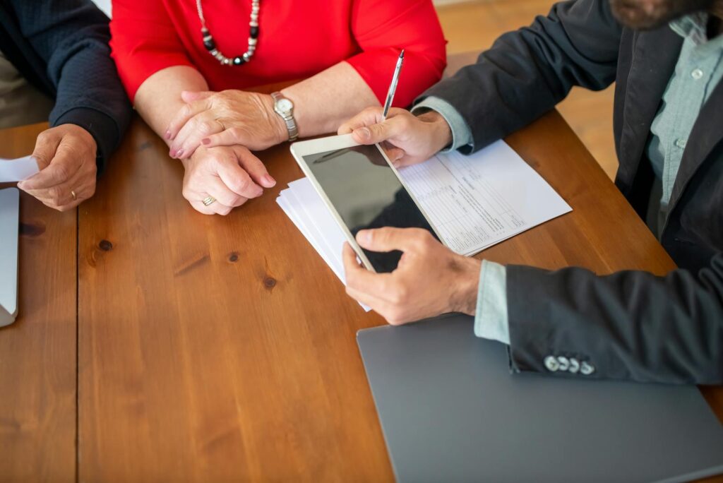 Réunion d'affaires à une table en bois avec un consultant examinant des documents et utilisant une tablette numérique.