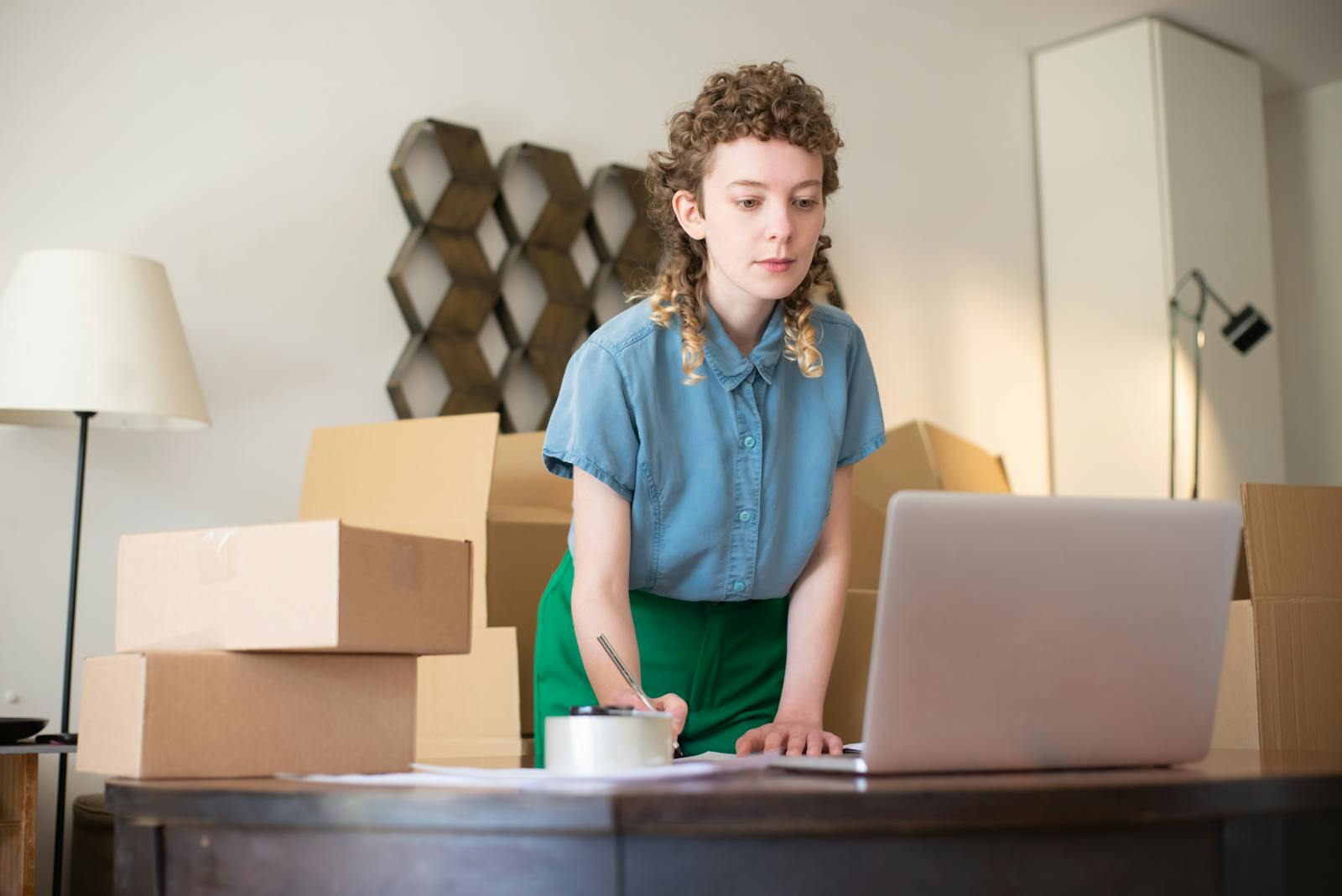 Une jeune femme travaillant sur son ordinateur portable, entourée de boîtes en carton, indiquant des activités commerciales en ligne.